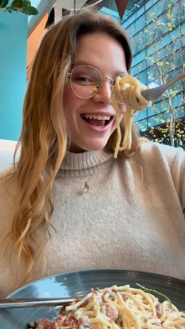 The video showcases a dining experience at Prezzo Italian restaurant. It features a young woman and a friend enjoying their meal. The video displays several dishes, including two orange cocktails (likely Aperol Spritz), fried mozzarella sticks in a red sauce, creamy baked mushrooms with bread, spaghetti carbonara, a baked rigatoni dish with chili, and a chocolate fudge cake with ice cream. The woman is shown eating the pasta and dessert, smiling and appearing to enjoy the food.