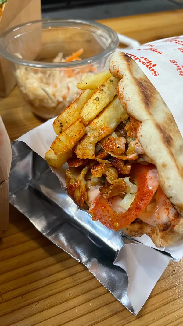 This video showcases a visit to Smashing Plates, a street food vendor located in Tooting Broadway Market.  The video highlights various menu items including a meat platter with skewers, halloumi, fries, and sauces; a chicken gyro; honey halloumi; and pita doughnuts. The food is presented in cardboard boxes and containers, with emphasis on the various components and colors.  No specific dietary information beyond the mention of vegan options is provided. The main focus is on showcasing the variety and visual appeal of the food.