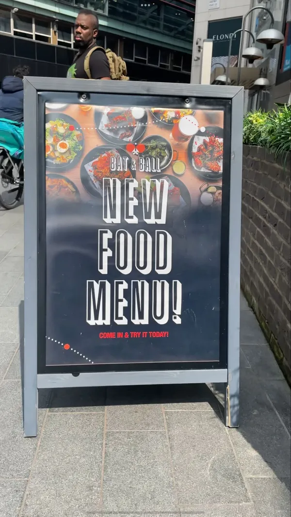 The video showcases Bat & Ball, a bar in Stratford, East London. It features various food items including pizzas (BBQ Pollo), burgers (Frying Nemo), crispy squid, Korean chicken wings, churros, and cheesecake. The drinks shown are cocktails (Zombie and Lady Luck) and beers (Guinness). The video also displays the venue's interior, including table tennis and pool tables, and shows a bartender making a cocktail.
