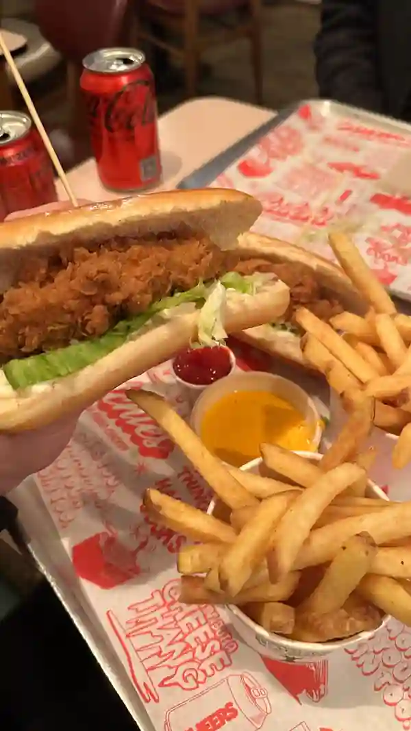 The video showcases a food review of the "Chicken Dawg" from Butchies, a buttermilk fried chicken restaurant in London.  The reviewer shows the sandwich being prepared, then adds cheese sauce, and also dips chips in the cheese sauce. The setting appears to be the restaurant itself. The sandwich is presented in a brioche roll, with lettuce and mayonnaise, and it has a crisp, golden-brown fried chicken tender.  The cheese sauce is visibly thick and rich, and the chips look golden brown and crispy. No dietary information is explicitly mentioned. The main focus is the food review and the tasting experience.