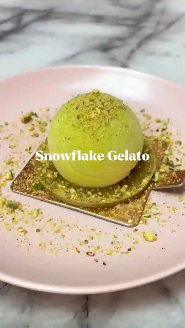 The video showcases Snowflake Gelato, a cafe in London, specializing in gelato-based desserts.  It features various items, including a Wimbledon-themed tennis ball gelato, gelato baskets, a gelato donut, milk cake pistachio, a praline Sunday shake, and an iced pistachio latte. The presentation emphasizes pastel colors, close-ups of textures, and overhead shots to highlight the food's appearance. No specific dietary information is provided.