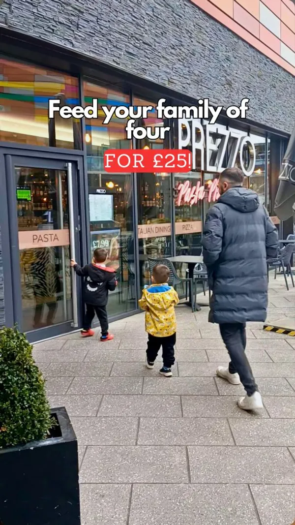This video promotes Prezzo's family bundle deal. It starts with two young boys entering the restaurant with an adult. Inside, one boy is shown coloring at the table, followed by a shot of the family bundle menu. The video shows the boys sitting at the table, followed by a cheers with a pink cocktail and a beer. A garlic bread appetizer is shown being cut and eaten by one of the boys. The main course of rigatoni bolognese is presented, and the boys are shown eating it with fries. The video concludes with the boys running out of the restaurant with the adult.