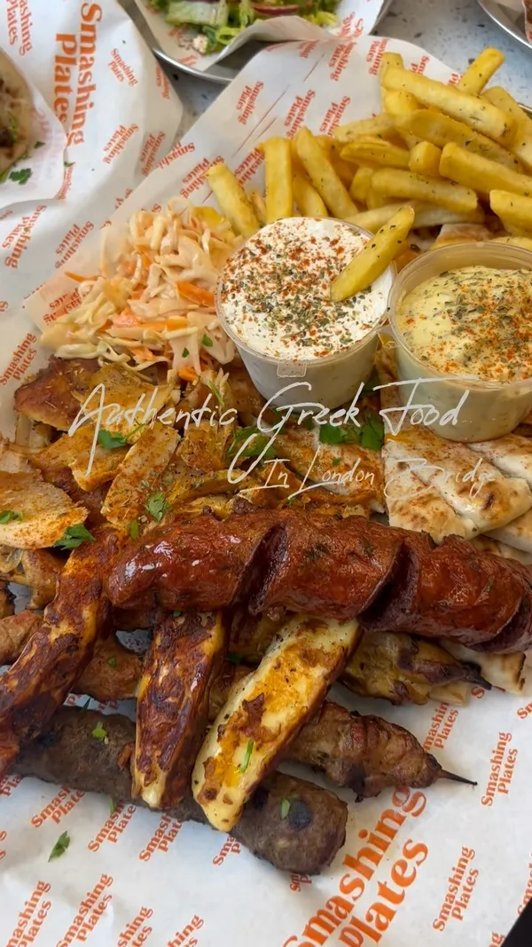 This video showcases Smashing Plates, a Greek restaurant in London Bridge.  The video features various dishes including a large sharing platter with grilled meats, sausages, fries, salads, and dips; a Greek salad; feta cheese fries; a gyro; and baklava. The food is presented attractively, with a focus on vibrant colors and textures. The setting is both inside and outside the restaurant, highlighting the inviting ambiance. No specific dietary information is mentioned.