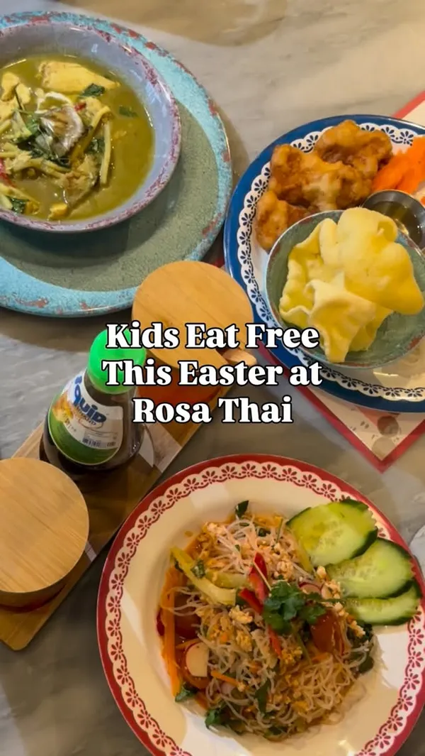 The video promotes a 'Kids Eat Free' Easter deal at Rosa Thai restaurant. It shows a variety of Thai dishes on a table, including a green curry, a glass noodle salad, and a kids' meal with noodles, fried chicken, and vegetables. The video features a young girl eating her meal and enjoying the restaurant experience, including a creative shot of her looking into the kitchen pass. The overall setting is a casual, modern restaurant interior.