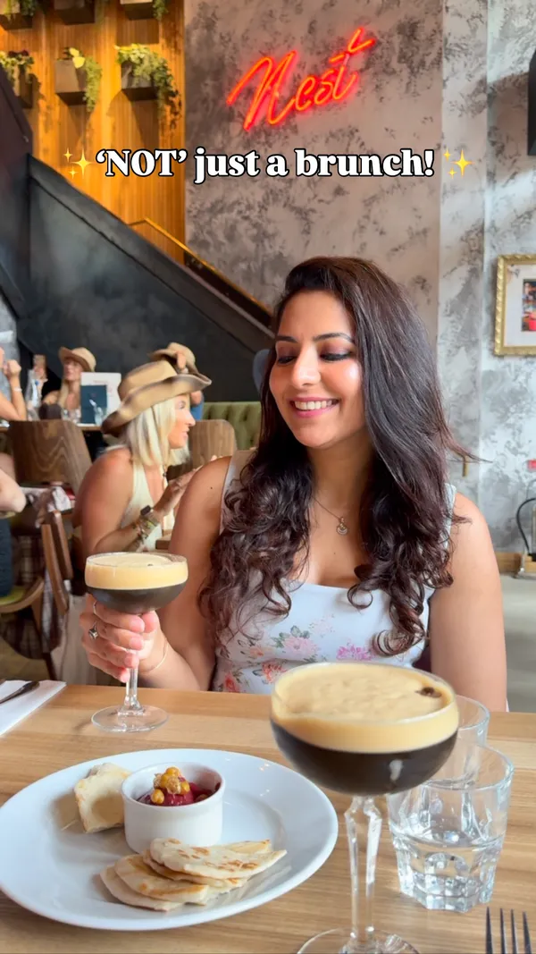 The video promotes a themed brunch event, the 'Texas Hold'Em Country brunch,' at The Nest restaurant in Bishopsgate, London. It showcases the lively and entertaining atmosphere, which includes drag queen performances, dancing, singing, and games, with many patrons wearing cowboy hats. The food and drinks featured include espresso martinis, a burger with fries, and chicken and waffles. The overall focus is on the fun 'vibe' of the event, positioning it as an ideal spot for a girls' brunch or hen party.