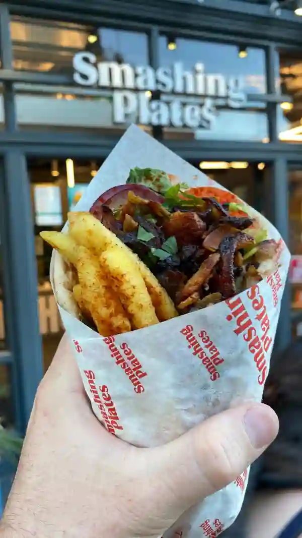 The video showcases various dishes from Smashing Plates, a street food establishment near London Bridge. It features a chicken gyros wrap, lamb and beef skewers, courgette and feta bites, unorthodox fries with pork gyros, and chocolate pittanuts.  The food is presented in close-up shots, emphasizing textures and colors. The main focus is a meal showcase.