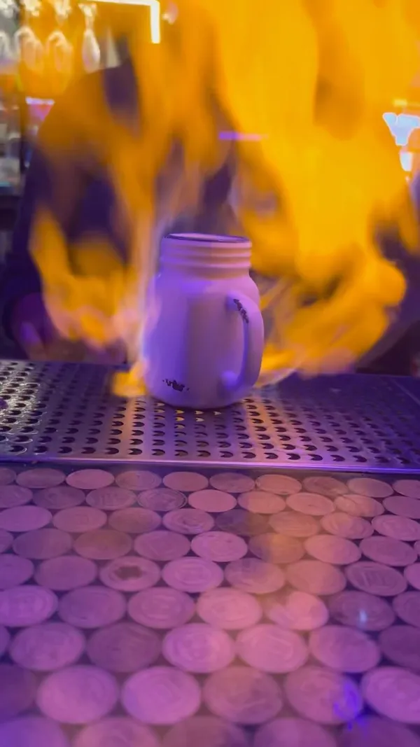 The video showcases NQ64, an arcade bar in Shoreditch. It features various cocktails (including one that's set on fire), and a wide array of arcade games, from retro classics to modern titles like Guitar Hero and Top Skater. The presentation emphasizes the vibrant atmosphere and fun, social aspects of the bar.