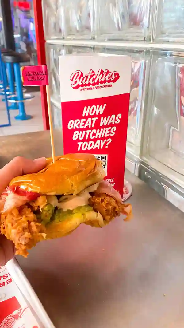 The video showcases Butchies Fried Chicken restaurant in London. It features various menu items including the Cheesy Rider and Jenny from the Block sandwiches, chicken wings, and fries.  The food is presented on trays and in close-up shots highlighting the textures and appearance. Dietary information isn't explicitly provided, but the menu does mention plant-based options. The main focus is on showcasing the food and the dining experience.