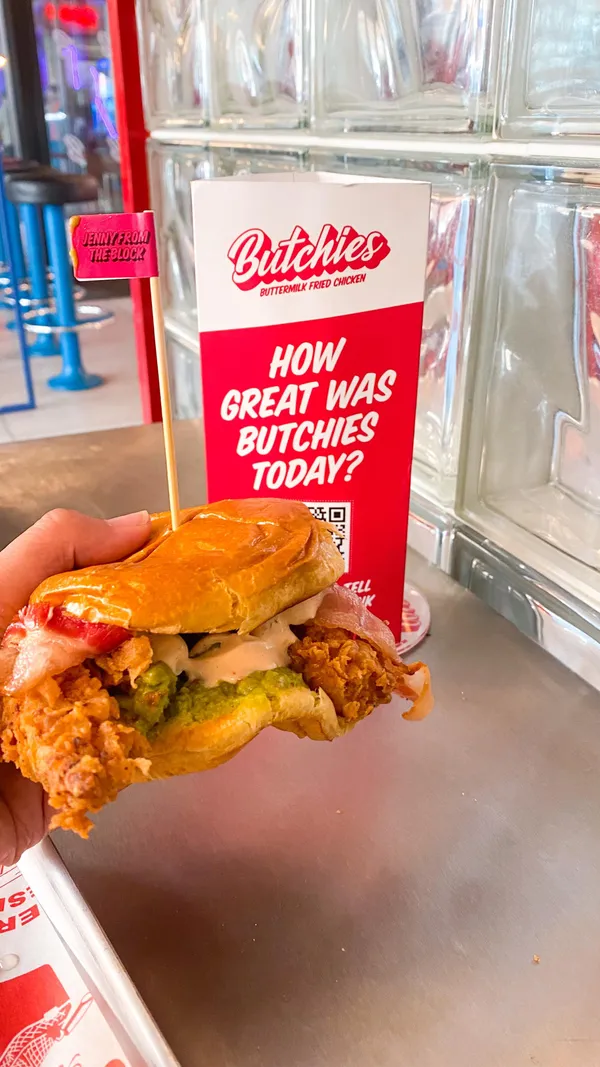 The video showcases Butchies Fried Chicken restaurant in London. It features various menu items including the Cheesy Rider and Jenny from the Block sandwiches, chicken wings, and fries.  The food is presented on trays and in close-up shots highlighting the textures and appearance. Dietary information isn't explicitly provided, but the menu does mention plant-based options. The main focus is on showcasing the food and the dining experience.