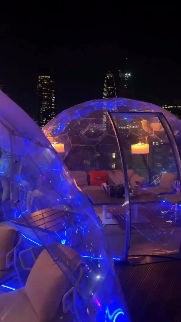 A fast-paced montage showcasing Circes Rooftop Bar in London at night. The video highlights the venue's unique features, including futuristic, illuminated private pods with city views, a stylishly lit indoor area, a well-stocked bar, and a photo booth. It also features a variety of small plates and cocktails, including pan-fried scallops, sliced steak, falafel, tempura calamari, sigara borek, tzatziki with bread, a Pornstar Martini, and a Negroni. The overall vibe is trendy, vibrant, and atmospheric.