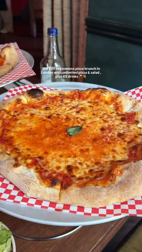 The video showcases a bottomless pizza brunch at a restaurant in Kensington, London. It features several close-up shots of different pizzas, including a Margherita, a pepperoni with ricotta, and one with jalapenos and olives. There are clips of a person taking a slice of pizza, a close-up of an orange cocktail (likely an Aperol Spritz) being stirred, and a brief wide shot of the restaurant's stylish interior. The main focus is on the variety and appeal of the pizzas available in the deal.
