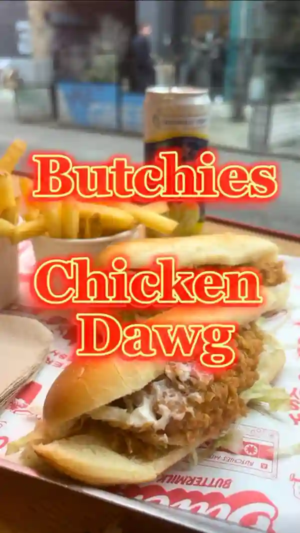 The video showcases Butchies Chicken Dawg, a new menu item from Butchies_london.  The setting is the restaurant itself, both exterior and interior shots are shown. The food shown includes two chicken dawgs (buttermilk chicken tenders, mayo, and lettuce in a brioche bun) and a side of fries.  A Sanpellegrino Limonata is also visible. The presentation focuses on close-ups of the chicken dawg, highlighting the texture and ingredients. No specific dietary information is provided. The main focus is on the food and the restaurant environment.