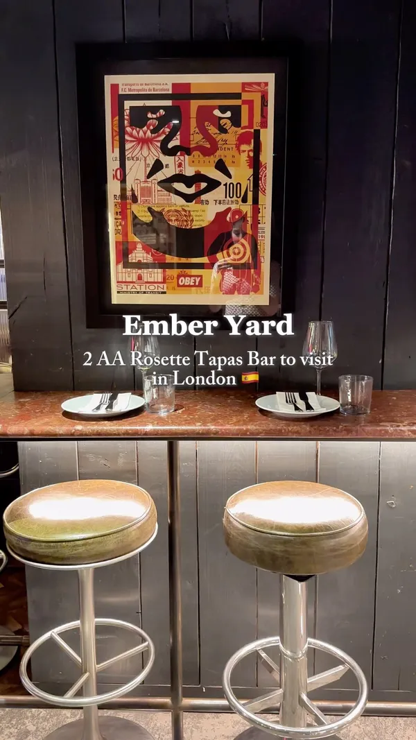 The video showcases Ember Yard, a tapas bar in London. It highlights the bar's ambiance, featuring various artistic wall decor and wooden furniture. The food showcased includes olives, roasted peppers, tomato salad, shrimp, asparagus, and a dessert with raspberries and ice cream. The drinks shown include a red cocktail. The presentation is modern and aesthetically pleasing. No dietary information is explicitly provided. The main focus is on showcasing the food, drinks, and ambiance of the bar.