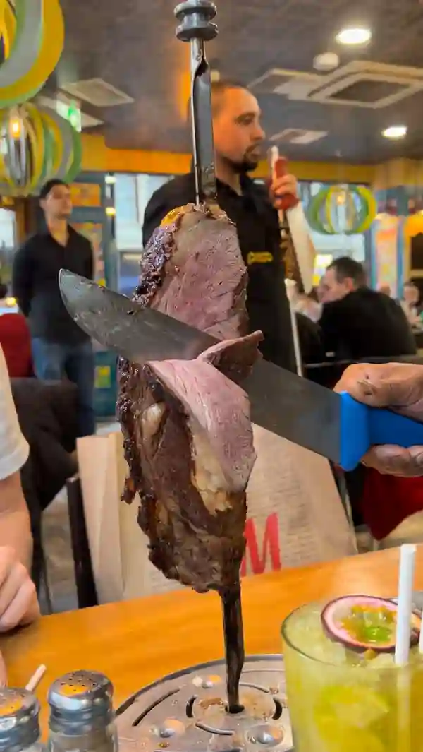 This video showcases Preto, a Brazilian steakhouse in London's West End.  It features various food items from their all-you-can-eat rodizio, including different cuts of grilled meats (steak, pork, chicken, chorizo), various side dishes (French fries, cheesy potatoes, salads), and desserts (mango mousse and coconut cake). The presentation emphasizes the abundance of food and the lively atmosphere of the restaurant.  The video highlights the 'I'm Full'/'More Please' card system.