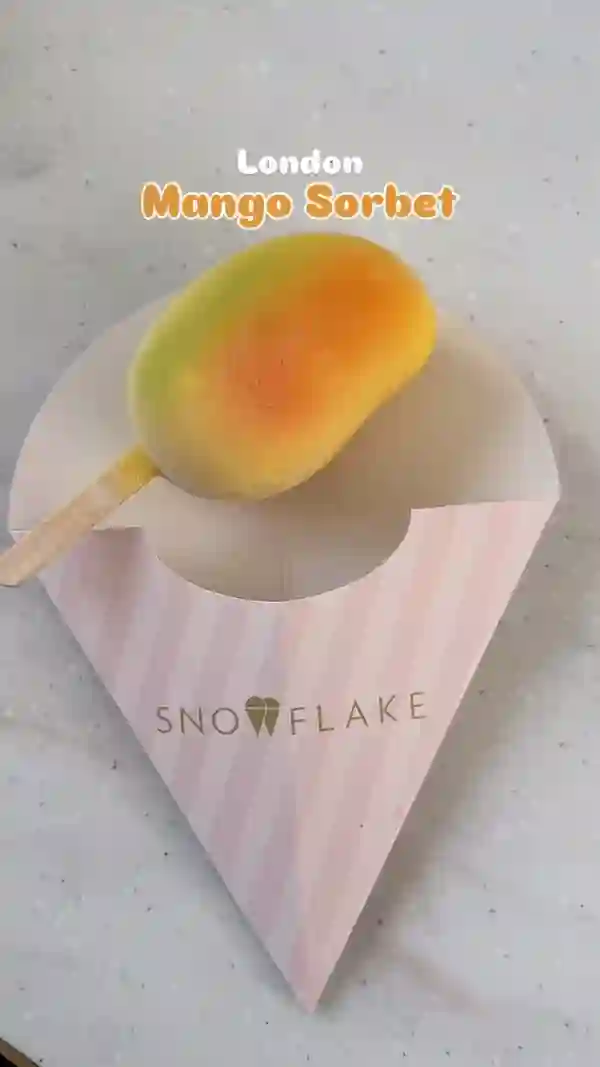 The video showcases mango sorbet on a stick from Snowflake Gelato in London. The sorbet is mango-shaped and features a colorful gradient.  The video shows the sorbet being eaten and also shows the gelato display case at the store.