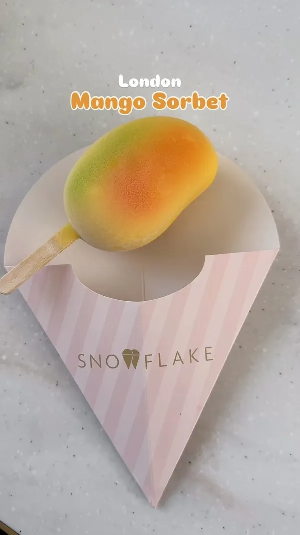 The video showcases mango sorbet on a stick from Snowflake Gelato in London. The sorbet is mango-shaped and features a colorful gradient. The video shows the sorbet being eaten and also shows the gelato display case at the store.