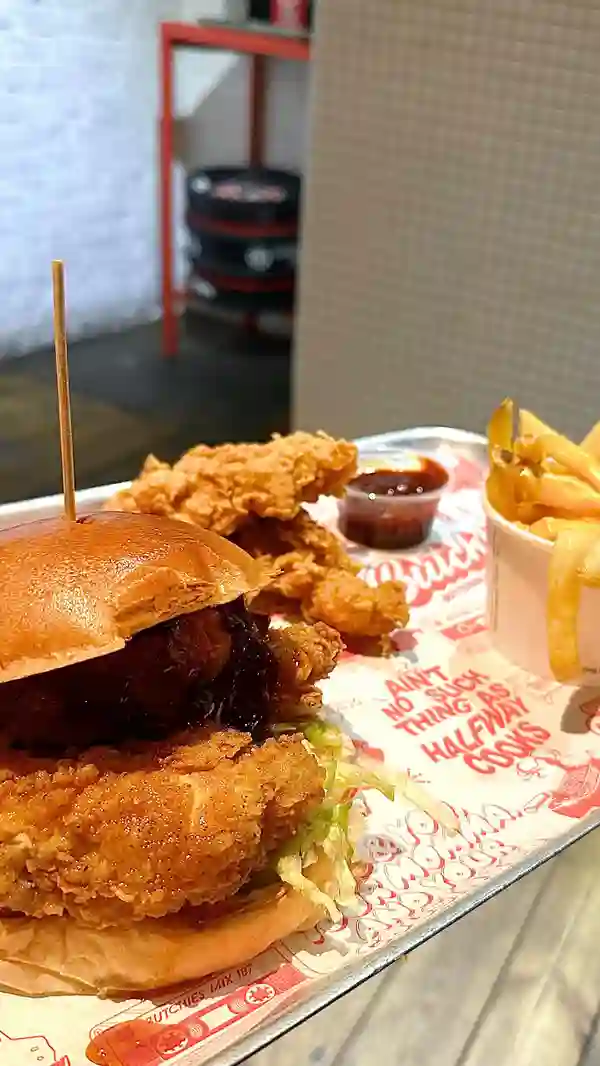 The video showcases a Christmas special, the Sweet Baby Cheesus burger, from Butchies Buttermilk Fried Chicken in London. The burger features chicken tenders, deep-fried camembert, cranberry sauce, chili honey, and pickles. The video also shows chicken tenders and cheese chips as sides. The presentation focuses on close-ups of the food and the influencer eating it. No specific dietary information is provided.