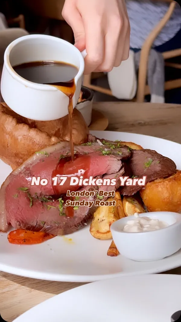 This video showcases a variety of food and drink options available at No 17 Dickens Yard in London. The video begins with a close-up shot of a roast beef dinner, transitioning to a wider view showing a table full of various meals and drinks, including a burger, steak, salmon dish, and cocktails. The video then offers shots of the restaurant's interior and exterior, highlighting the ambience and location.  Menu items such as a fried chicken burger, steak, and sweetcorn and courgette hash are featured. The video emphasizes the restaurant's Sunday roast as a highlight.