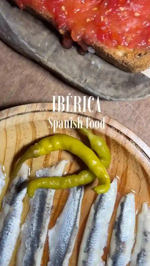 This video showcases a meal at IBÉRICA, a Spanish restaurant by Nacho Manzano. It features various tapas and dishes, including anchovies, tomato bread, jamón, croquettes, garlic prawns, aubergine sobrasada, mussels in vermouth sauce, black rice with seafood, and vanilla caramel flan. The food is presented beautifully, with close-up shots highlighting textures and details. The video is primarily focused on showcasing the restaurant's food and atmosphere.