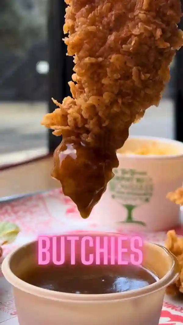 The video showcases a variety of fried chicken dishes from Butchies, a restaurant with multiple London locations.  The video uses a point-of-view (POV) perspective to show a customer dipping a chicken tender into a sauce. It also features a wider shot of a tray filled with fried chicken tenders, fries, cheese sticks, mac and cheese, and a burger. The food is presented in a visually appealing way with high-quality close-up shots. No specific dietary information is provided.