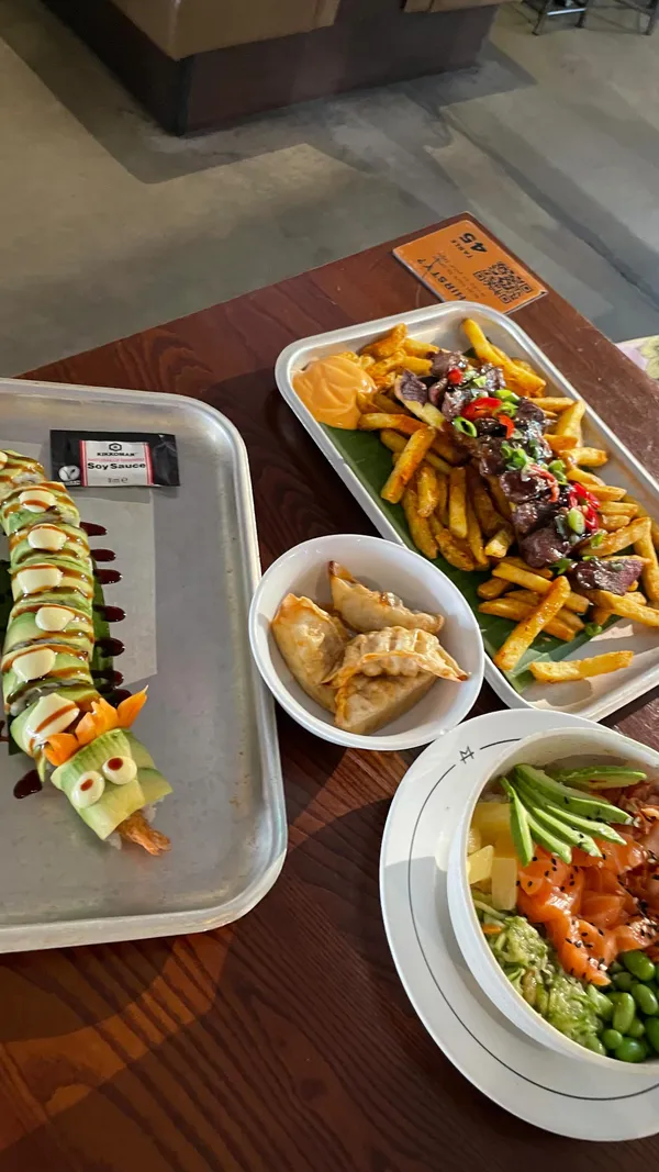 The video showcases Inamo Sukoshi, a Japanese fusion restaurant located within Market Halls, a food hall near Oxford Circus in London. It features various dishes, including a steak with teriyaki marinade and fries, pork gyoza, a salmon poke bowl, and a dragon roll (sushi). The food is presented appealingly, with a focus on vibrant colors and visually interesting arrangements, particularly the dragon roll's design. The video appears to be a sponsored post or PR collaboration.