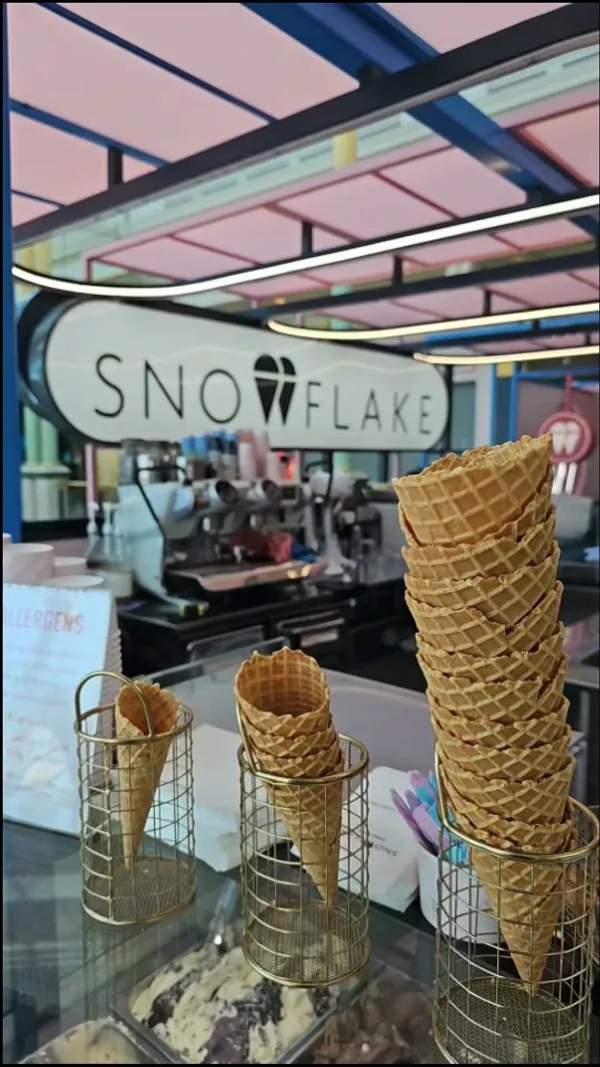 The video showcases Snowflake Gelato, a cafe located in a bright shopping mall. It highlights various gelato flavors, iced pistachio lattes, cookies, marshmallows, chocolate-covered strawberries, and other sweet treats. The presentation emphasizes vibrant colors, close-ups of textures, and the overall aesthetic of the cafe. No dietary information is explicitly mentioned.