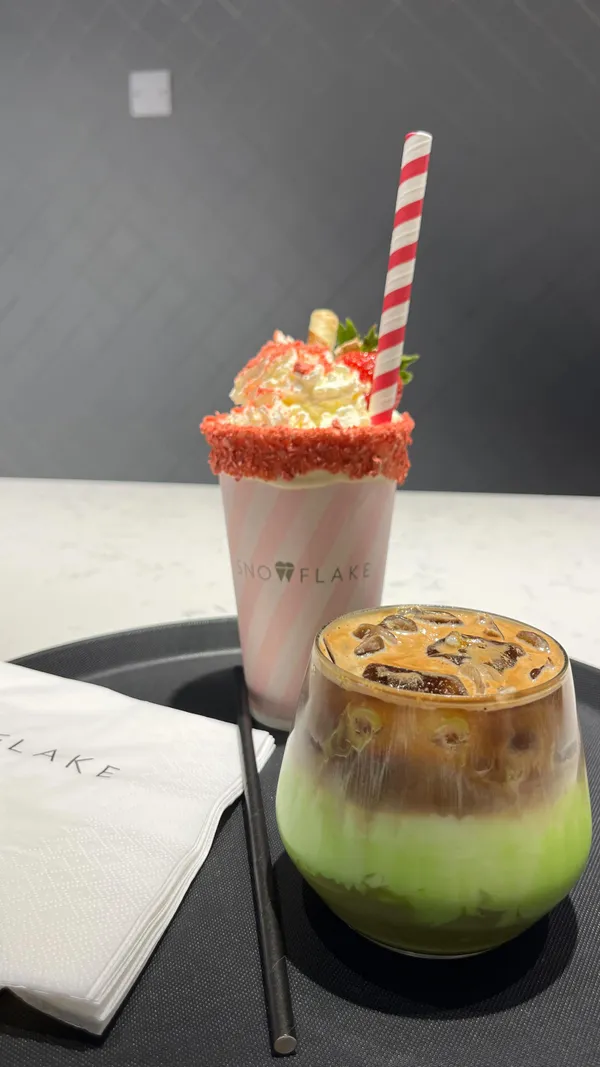 The video showcases Snowflake, a gelato and coffee shop located at the 02 in Greenwich, London.  It features various desserts, including gelato in cones and cups with different flavor combinations, a strawberry sundae milkshake, and an iced pistachio latte. The presentation emphasizes the vibrant colors and creamy textures of the gelato and the appealing visual presentation of the drinks and desserts.  No specific dietary information is provided.
