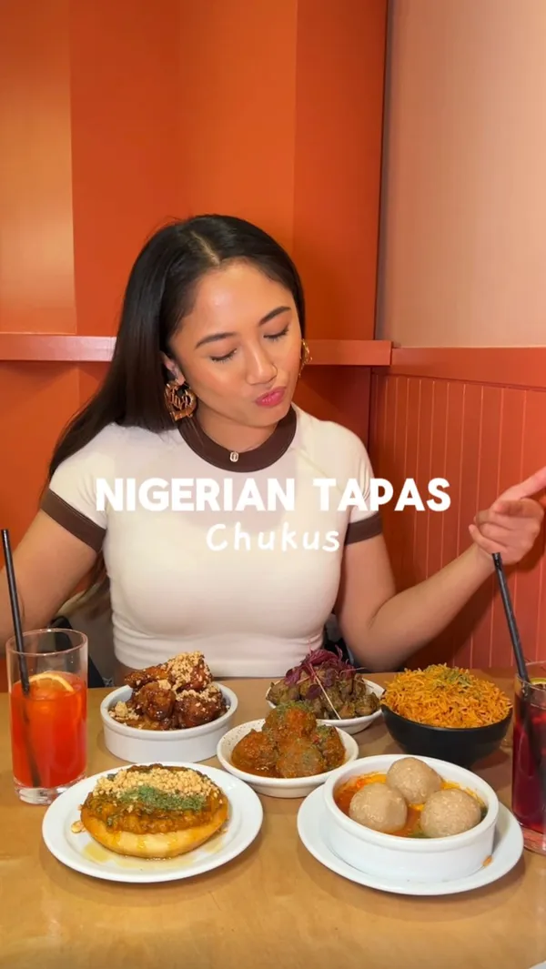 The video showcases a meal at Chuku's, a Nigerian tapas restaurant in Tottenham, London. The influencer samples a variety of dishes, including Suya Meatballs, Lamb Ayamase, Caramel Kuli Kuli wings, Sinasir & Miyan Taushe, Egusi Bowl, and Jollof Rice, alongside two cocktails, Eze and Chapman Punch. The food is presented in small bowls and plates, arranged attractively on a table. Dietary information is not explicitly given for each dish but the caption mentions vegan, gluten-free and halal options. The primary focus is on the food and drink, with the influencer expressing her enjoyment of each item.