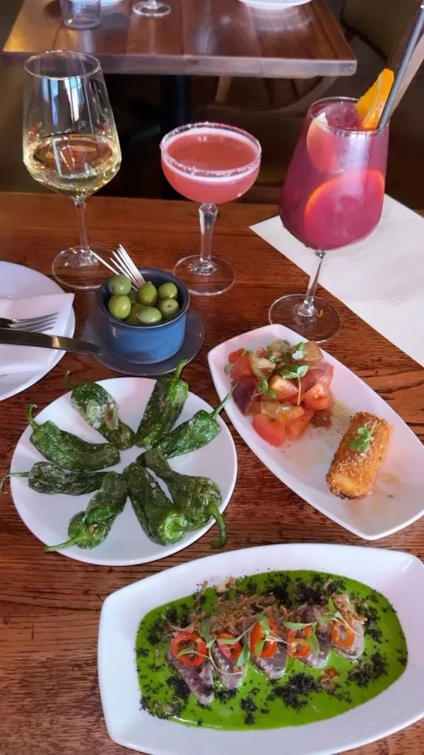 This video showcases Ember Yard, a Spanish and Italian tapas restaurant and bar in Soho, London. It features a tasting menu, highlighting various dishes such as pan-fried prawns, yellowfin tuna, heirloom tomato salad, grilled secreto ibérico, grilled asparagus, rubia gallega pinchos, padrón peppers, and olives.  The video also shows cocktails (Smoky Hibiscus Margarita and Sangria) and a dessert (coffee cheesecake). The presentation emphasizes close-ups of the food and drinks, focusing on colors, textures, and plating.  No specific dietary information is provided besides the vegan aioli option with asparagus. The main focus is showcasing the food and ambiance of the restaurant.