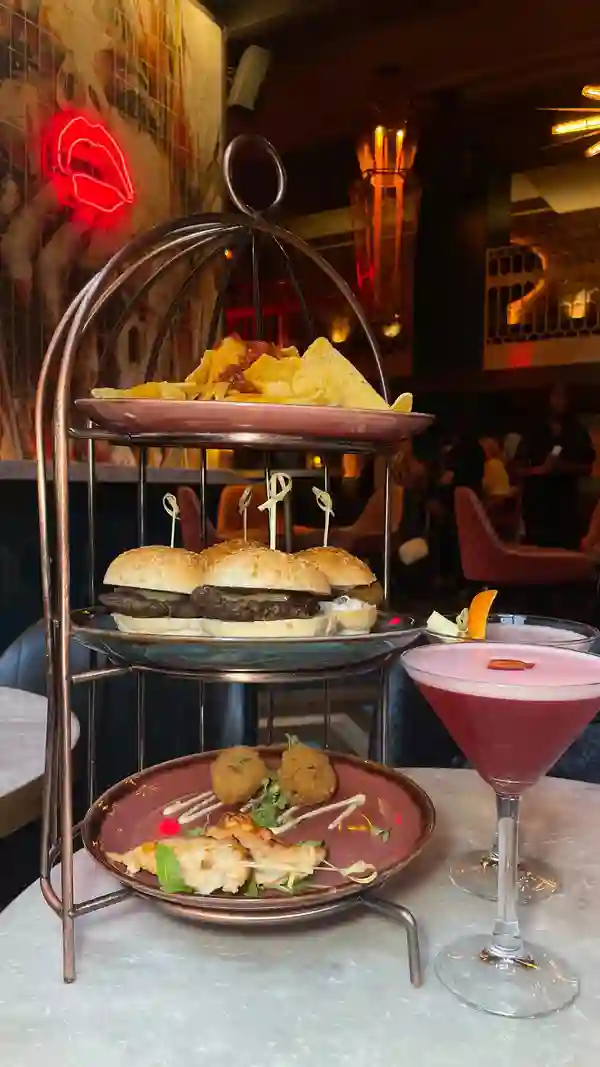 The video showcases a bottomless brunch experience at Dirty Martini in Birmingham, UK. It features a three-tiered food stand with nachos, mini burgers, and chicken skewers, along with pink cocktails. The setting is a stylish bar with a vibrant atmosphere. The video highlights the cocktails, the food, and the overall ambiance of the venue.