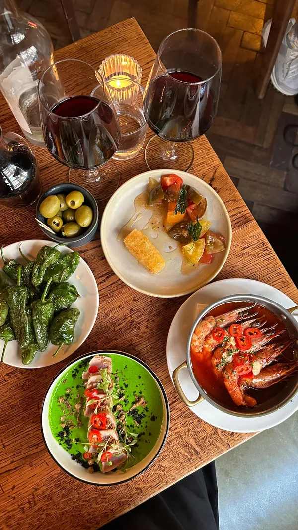 The video showcases Ember Yard, a modern tapas restaurant in London, offering a blend of Italian and Spanish cuisine. It features various dishes, including grilled prawns, patatas bravas, a steak dish, tuna sashimi, and a dessert mille-feuille. The food is presented aesthetically, with close-ups highlighting textures and colors. The ambiance is shown through shots of the restaurant's interior, including its bar area and dining space. The video focuses on the dining experience and the food quality.