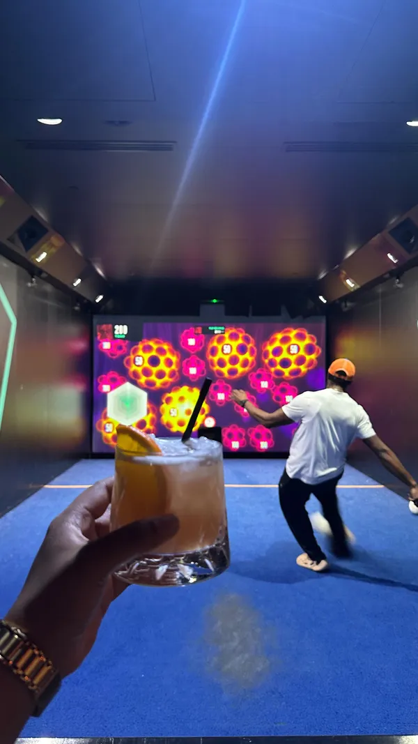 The video showcases a couple's date night at Toca Social, a venue that combines dining with interactive football-themed games. The video begins with the couple entering the venue, followed by clips of them playing a football game that involves kicking balls at a screen. The woman narrates their experience, highlighting her initial skepticism about her partner's skills and her own playful trash talk. The video also features close-ups of the food they ordered, including wings and pigs in blankets, as well as mocktails. The video concludes with a photo booth session.