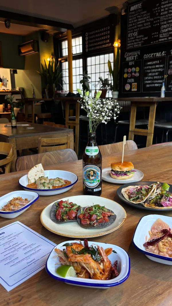 The video showcases a meal at the Magic Momo pop-up restaurant at The King and Co. in London. The setting is a casual, trendy restaurant.  Various dishes are shown, including momos (dumplings) in a sauce, apricot-glazed tiger prawns, a pomelo salad, watermelon tostada, a monkfish slider, khao soi roti, and a dessert of shortbread with tonka bean creameux and summer berries. The presentation is visually appealing, with close-ups of dishes.  Some dietary information is included by mentioning the availability of veggie and vegan options. The main focus is a food showcase of the Magic Momo popup menu.