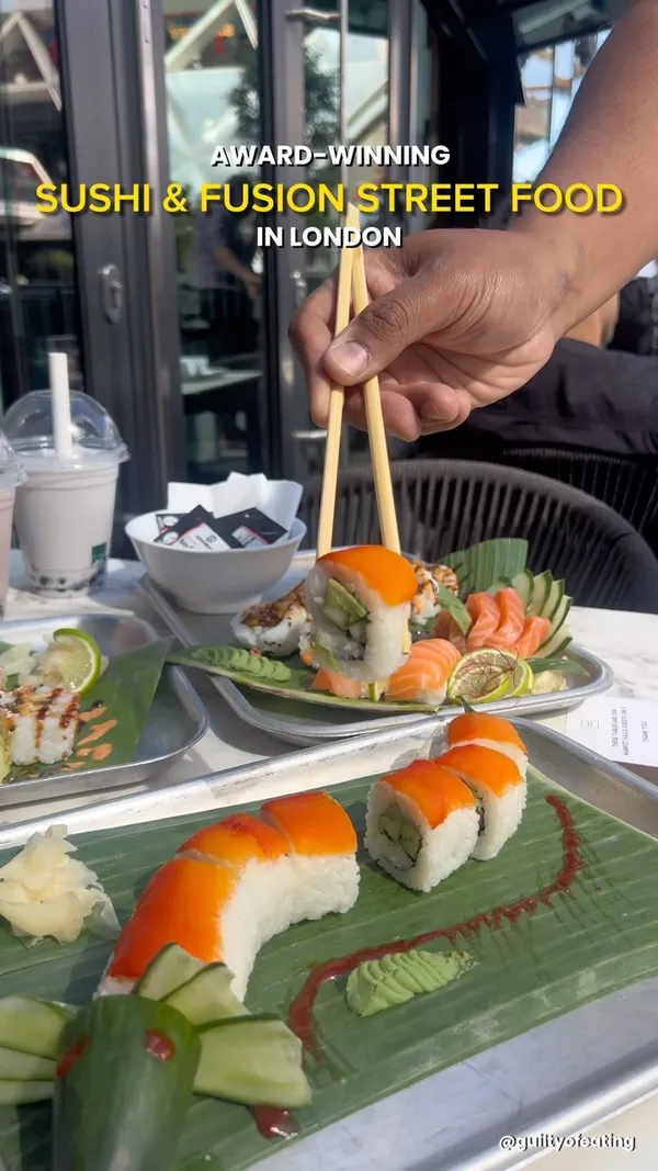 The video showcases Inamo Sukoshi, a sushi and fusion street food restaurant located in Market Halls Cargo, London. It features various sushi rolls (Crunch Salmon, Red Dragon Roll, Simply Salmon), sashimi, and bubble tea (Taro and Brown Sugar). The food is presented on banana leaves on sleek metal trays. Dietary information includes mention of non-halal meat (with a separate sushi counter) and vegan options. The main focus is on showcasing the visually appealing food and drinks.