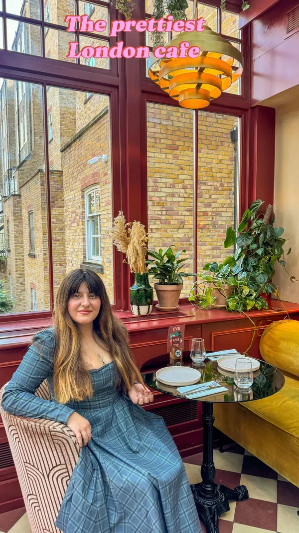The video showcases the interior of a restaurant, highlighting its natural light, decor, and food offerings. It features a long wooden table set for dining, a round table with chairs, and various plants and decorative items. The food shown includes two pizzas with different toppings (one with pepperoni, one with sausage, red onion, and tomatoes) and a side of fries. A woman is seen sitting at a table, enjoying the pizza. A drink is prepared and poured into a glass. The main focus is on presenting the restaurant as a visually appealing and enjoyable dining location.