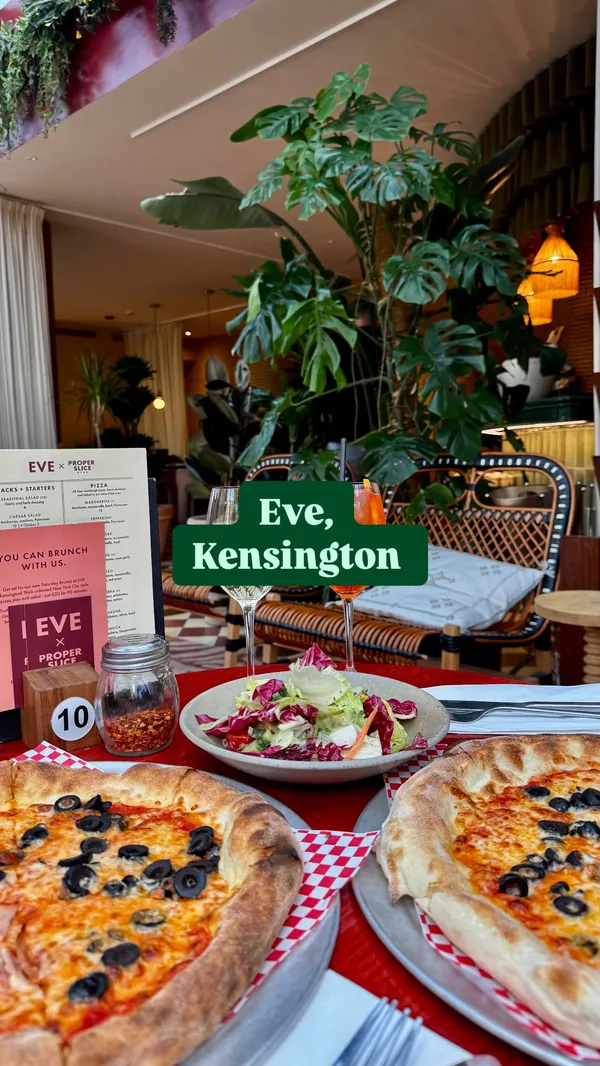 The video showcases the interior of Eve Kensington, a restaurant/bar, highlighting its stylish decor and conservatory area. It features a new Saturday brunch offer with unlimited New York City style pizza and salad for £20 for 90 minutes, with £5 drinks available. The video shows two pizzas (one with ham and olives, one with olives and artichoke), a side salad, wine, and an Aperol Spritz. It includes close-ups of the food and drinks, a shot of the menu/offer card, and hands clinking glasses.