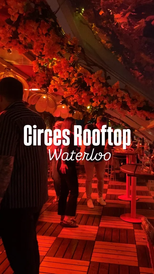 Video shows a lively rooftop venue with red lighting and people dancing. Features close-ups of food items including chips, falafel wraps, and garlic prawns. Also shows various drinks including frozen cocktails with cherries and striped straws, and shots. The video highlights the atmosphere and offerings of the venue.