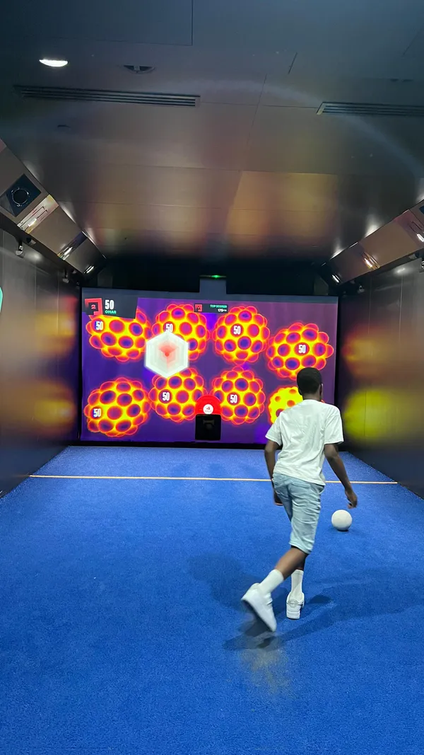 The video showcases Toca Social, an entertainment venue in Greenwich, London.  It features various interactive football games projected onto large screens.  The games involve kicking balls at targets to earn points. The venue's ambiance is dark with neon lighting. Food and drinks are mentioned as available, including a kids' menu, but not explicitly shown. The main focus is on the interactive football games and the fun experience at Toca Social.