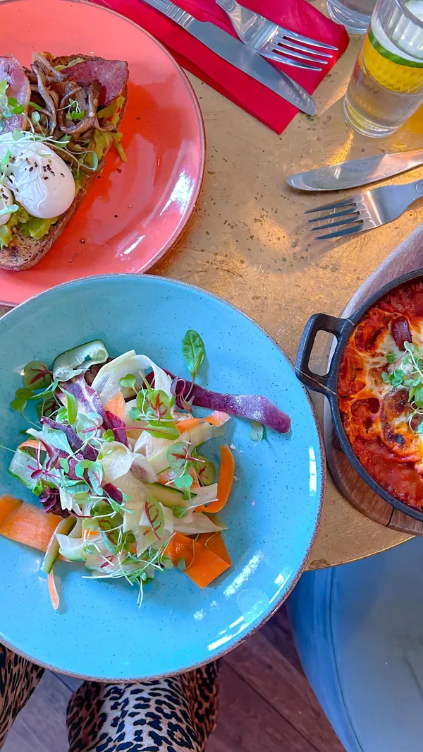 This video showcases The Little Orange Door, a restaurant and bar in Clapham, London.  It features various areas of the venue, including the bar, seating areas, and even a bathroom with unique decor. The food showcased includes avocado toast with poached eggs, a vibrant raw vegetable salad, and a baked eggs dish in tomato sauce. Drinks shown include orange juice and a sparkling beverage.  The presentation is colorful and emphasizes the cozy atmosphere. Gluten-free options are mentioned. The video primarily focuses on highlighting the restaurant's unique ambiance and food offerings.