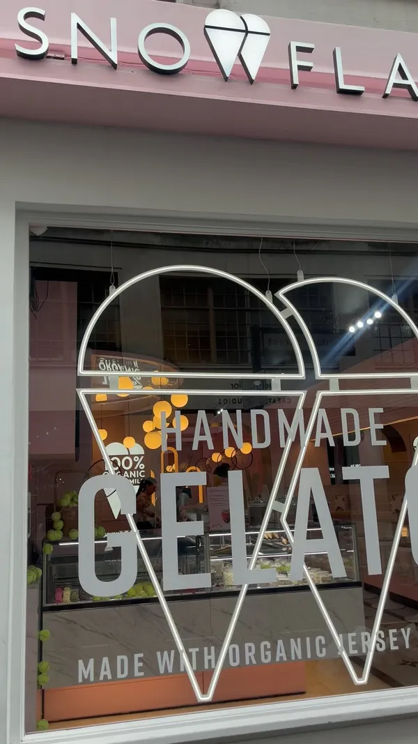 The video showcases Snowflake Gelato, a cafe offering gelato, waffles, and milkshakes.  The setting is a modern, pink-themed cafe with marble countertops and stylish decor.  Food and drinks shown include various gelato flavors, uniquely-designed tennis ball-shaped pastries, waffles with strawberries and chocolate sauce, and a milkshake with whipped cream and nuts. The presentation is visually appealing and well-lit, with a focus on aesthetically pleasing colors and arrangements. No dietary information is explicitly given. The main focus is a tour of the cafe and its offerings.