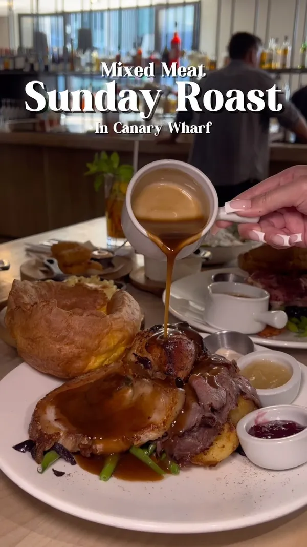 The video showcases a Sunday roast meal at No.35 Mackenzie Walk, a restaurant in Canary Wharf, London. The food includes a mixed meat roast (pork belly, roast chicken, and beef), Yorkshire pudding, mac and cheese, and various side dishes and sauces. The drinks include a Pimms Lemonade and orange juice. The video focuses on the appetizing visuals of the food and drink, with a cheerful and positive tone.