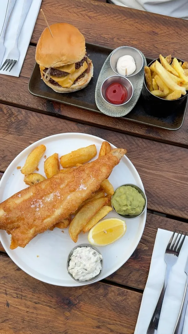The video showcases a pub that has recently reopened after a refurbishment. It features various food items including fish and chips, a burger, steak, ribs, coleslaw, and a dessert with strawberries and cream. It also shows drinks being toasted and highlights the pub's outdoor garden area with seating and a BBQ shack.