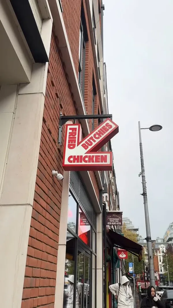 The video showcases Butchies Fried Chicken, a restaurant in London. It features various menu items, including a burger with chicken tenders and cheese sauce, chicken wings, and cheese fries. The food is presented on trays and in individual containers, highlighting the crispy textures and generous portions. The video focuses on the food's visual appeal, particularly the chicken's golden-brown color and the melted cheese. Dietary information isn't explicitly provided.