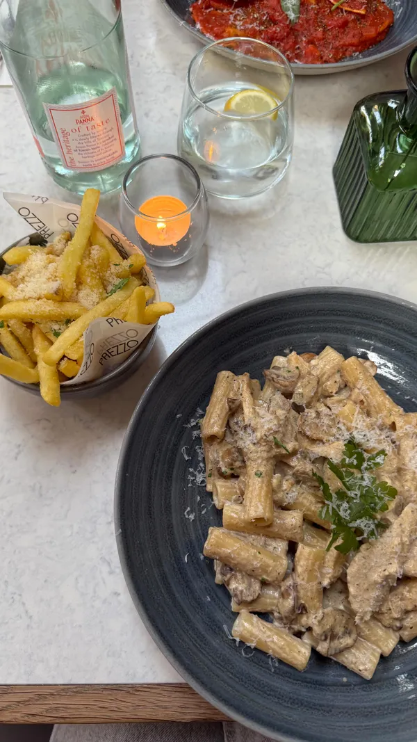 The video promotes Prezzo Italian restaurant and its new Club Prezzo app. It begins with a close-up of Nutella doughnut balls being dipped in chocolate, highlighting that they can be obtained for free by downloading the app. The video shows the exterior of the restaurant, the menu, and various dishes ordered, including a dough twist, oven-baked king prawns, crispy fried mozzarella (with a cheese pull), chicken, mushroom & garlic rigatoni, beef shin ravioli, truffle fries, and the free Nutella doughnut balls. The creator explains the benefits of the Club Prezzo app, such as special prices and birthday rewards. The video concludes with a shot of a Margherita pizza in a takeaway box.