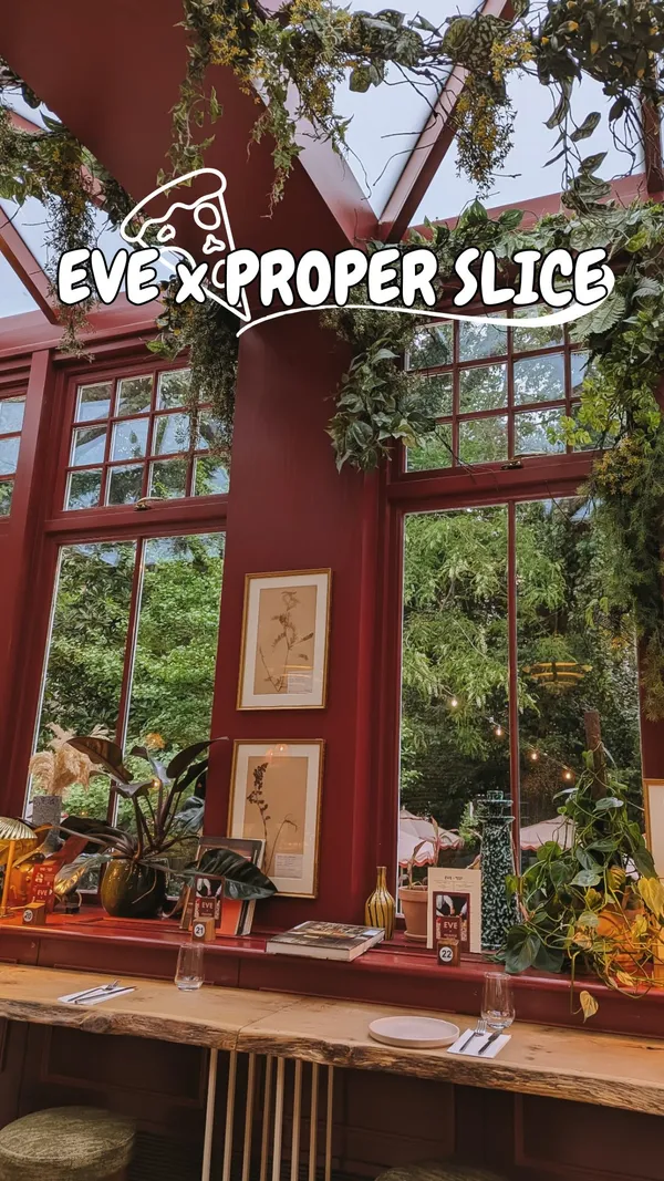 The video showcases the EVE x Proper Slice restaurant. It begins with an exterior shot of the entrance, followed by interior views showing the seating area and large windows. It features close-ups of drinks (rose wine and an Aperol Spritz-like cocktail), a burrata dish with pesto and basil, and two different pizzas (one with pepperoni/burrata and basil, another with olives, peppers, artichoke, and pepperoni). The video includes a shot of someone cutting into the burrata.