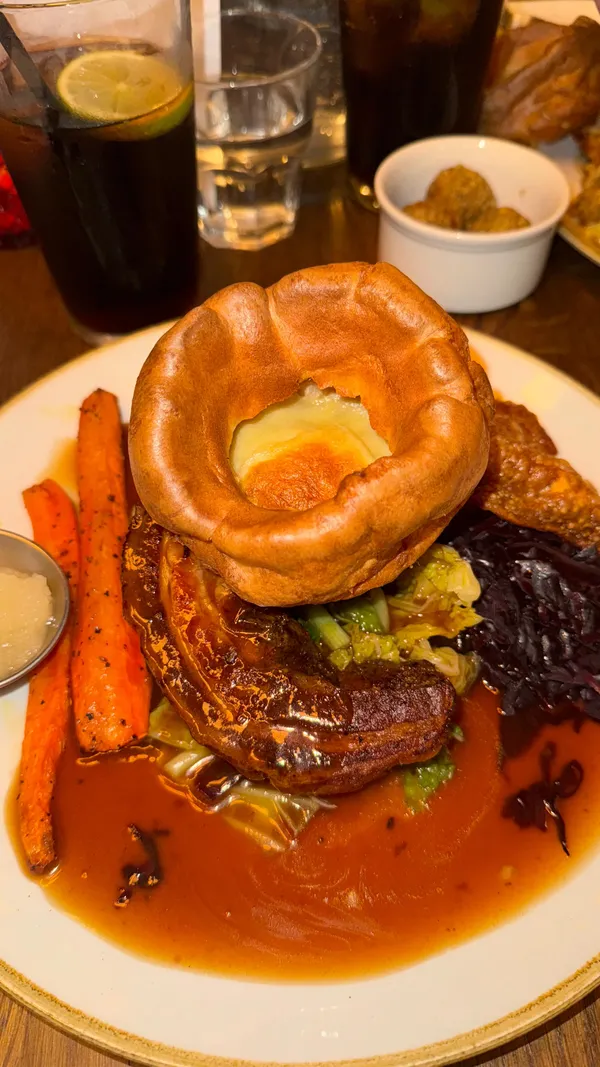 The video showcases Eltham GPO, a dog-friendly pub in South East London, highlighting their Sunday roast. It features shots of the pub's exterior and interior, the menu, a dog enjoying the atmosphere, and several close-ups of a delicious-looking pork belly roast dinner, including roast potatoes, Yorkshire pudding, and various vegetables.  The roast includes beef, chicken, pork, and vegan wellington options.