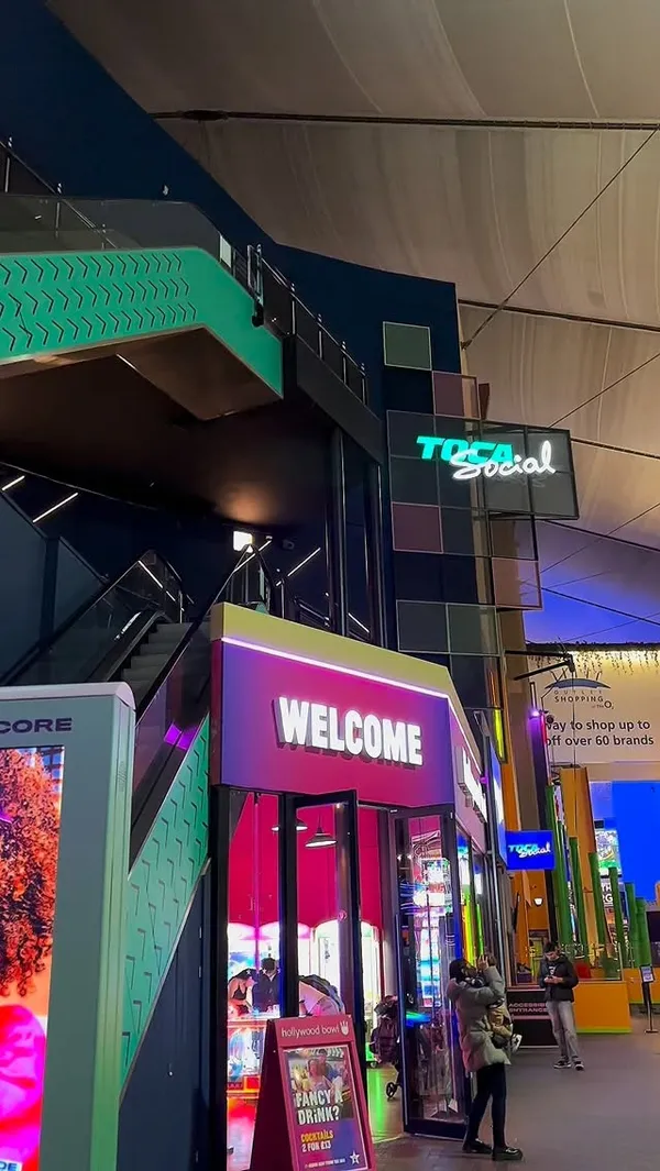 The video showcases a visit to Toca Social at the O2 in London. It begins by showing the entrance and then transitions into a montage of people playing various interactive football games on large screens. The games involve kicking footballs at digital targets, including zombies and scoring points. After the games, the video features the food and drinks available, displaying several trays with burgers, bacon, fries, coleslaw, and BBQ chicken wings. It also highlights a range of festive cocktails, garnished with rosemary, candy canes, and cinnamon sticks. The overall theme is a fun, social activity combined with casual dining and drinks.