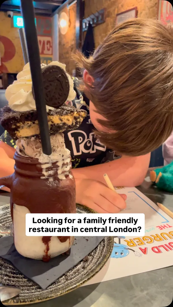 This video promotes Maxwell's Bar and Grill in Covent Garden, London, as a family-friendly restaurant. It begins with a close-up of a large, decadent 'freakshake' milkshake. The video then shows the exterior and interior of the restaurant, highlighting its 'cool vibes' with brick walls and retro decor. Various dishes are showcased, including sizzling shrimp fajitas, a large burger with fries, mac and cheese, a side salad, and BBQ ribs. The video features children at the table, reinforcing the family-friendly theme, and concludes with a shot of the restaurant's entrance.