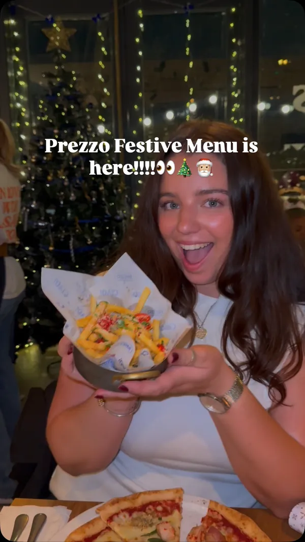 The video showcases the festive menu at a Prezzo Italian restaurant. It begins with an exterior shot of the restaurant at night, then moves inside to show two women enjoying festive drinks. The video highlights several dishes: Hot Honey Mozzarella Sticks with a prominent cheese pull, Tuscan Sausage & Brie Garlic Bread, Christmas Carbonara with turkey and pigs in blankets, Garlic Chilli Cheese Fries, a Christmas Pizza, and a trio of desserts including Sticky Toffee Pudding, Biscoff Cheesecake, and Tiramisu. The video ends with shots of promotional materials and festive decorations.