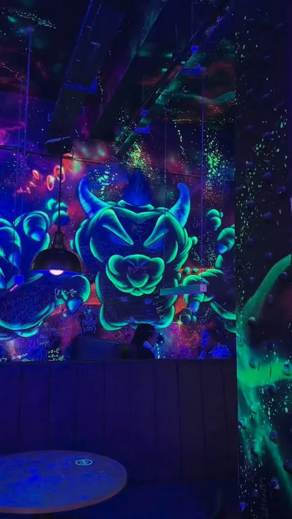 A montage video showcasing a date night at NQ64, a retro arcade bar. The setting is dimly lit with vibrant neon and blacklight graffiti. The video features a couple playing various arcade games like driving simulators, pinball, and light gun games. It also highlights the bar's creative, themed cocktails, including one with a Mario & Peach sticker, another being prepared with a blowtorch by a bartender, and a third served in a pouch with a light-up ice cube.